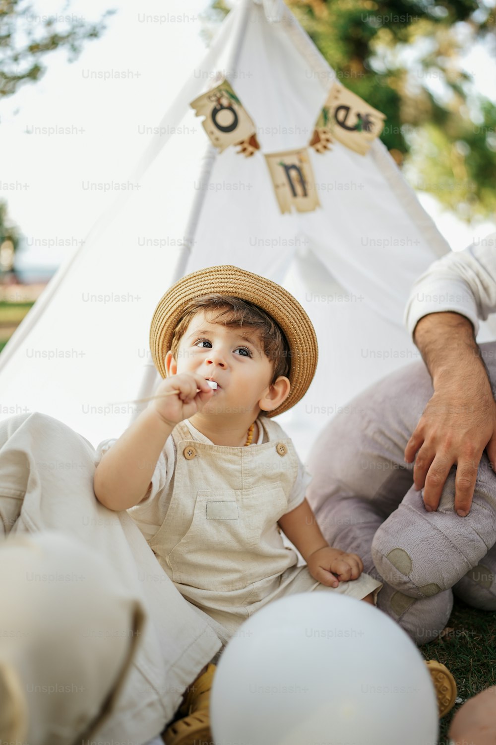 a little boy sitting on the ground in front of a teepee