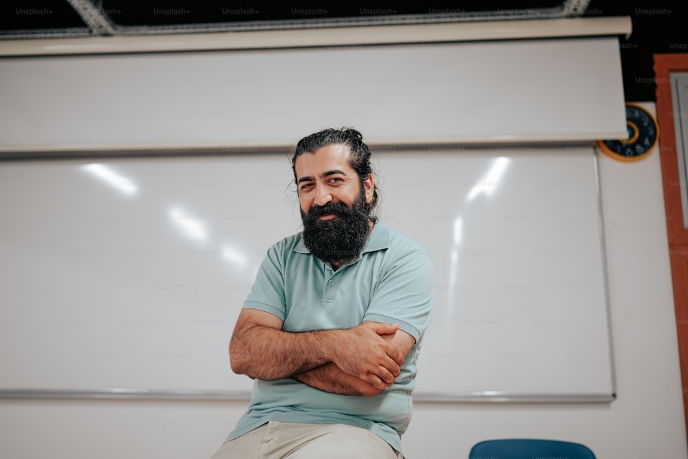 a man with a beard sitting in front of a whiteboard