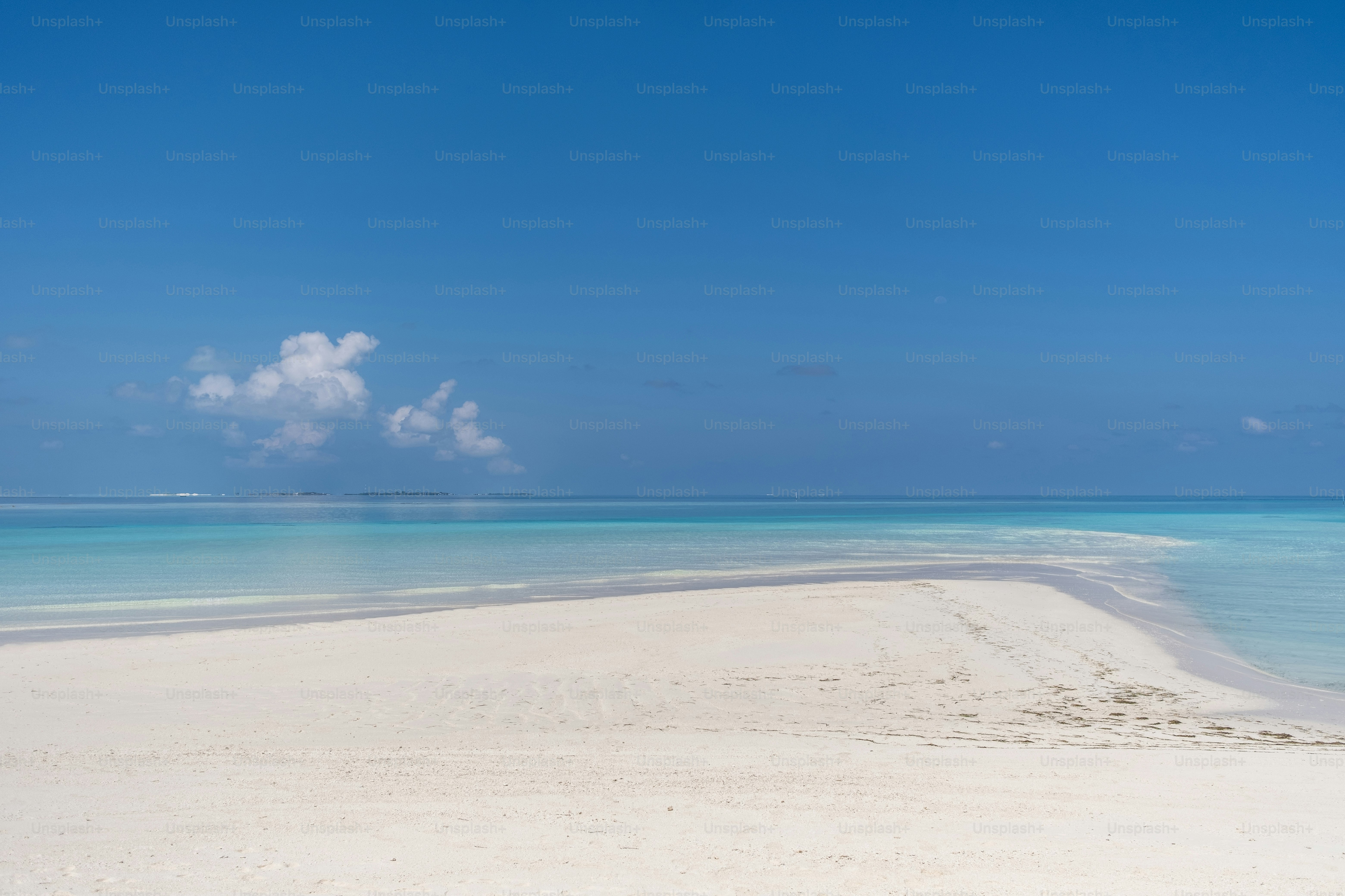 澄んだ青い水と空に雲が広がる砂浜