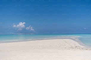 uma praia de areia com água azul clara e uma nuvem no céu