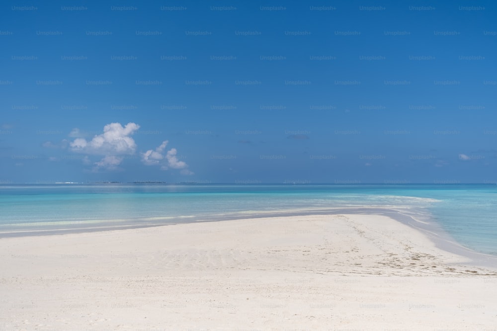 a sandy beach with clear blue water and a cloud in the sky