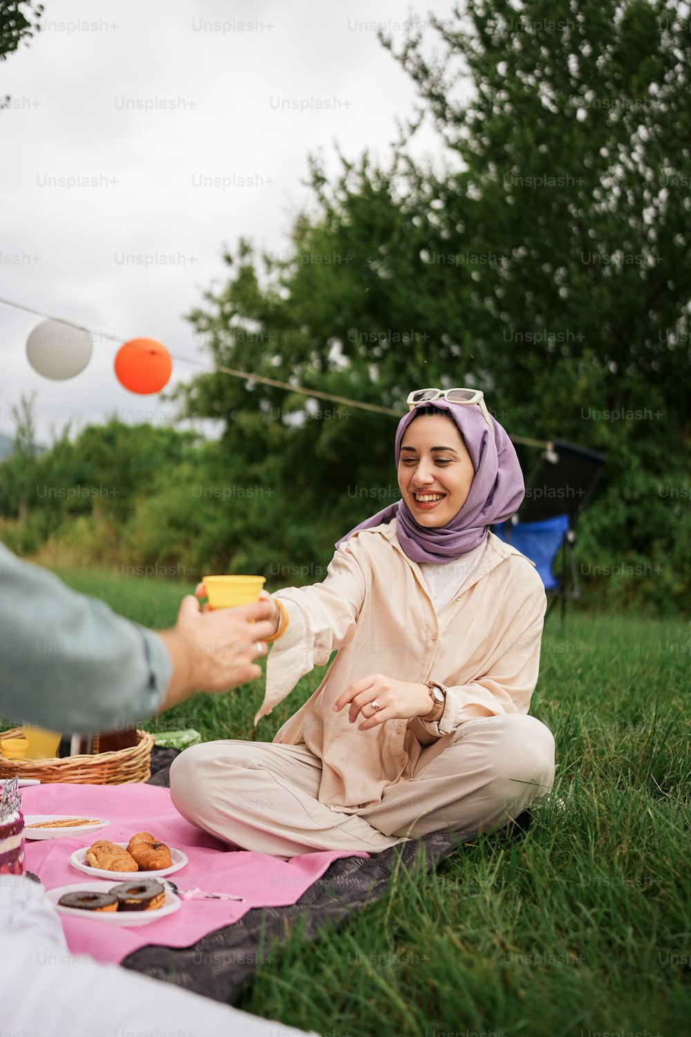 a woman in a hijab sitting on a blanket in the grass