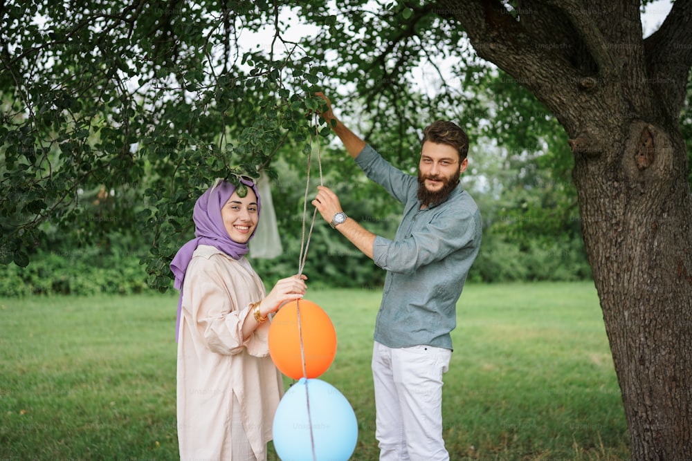 a man and a woman holding balloons in front of a tree