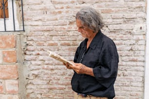 a man standing in front of a brick wall reading a book