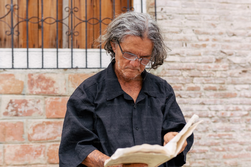 a man reading a book in front of a brick wall