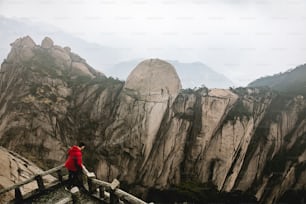 a man in a red jacket standing on a wooden bridge