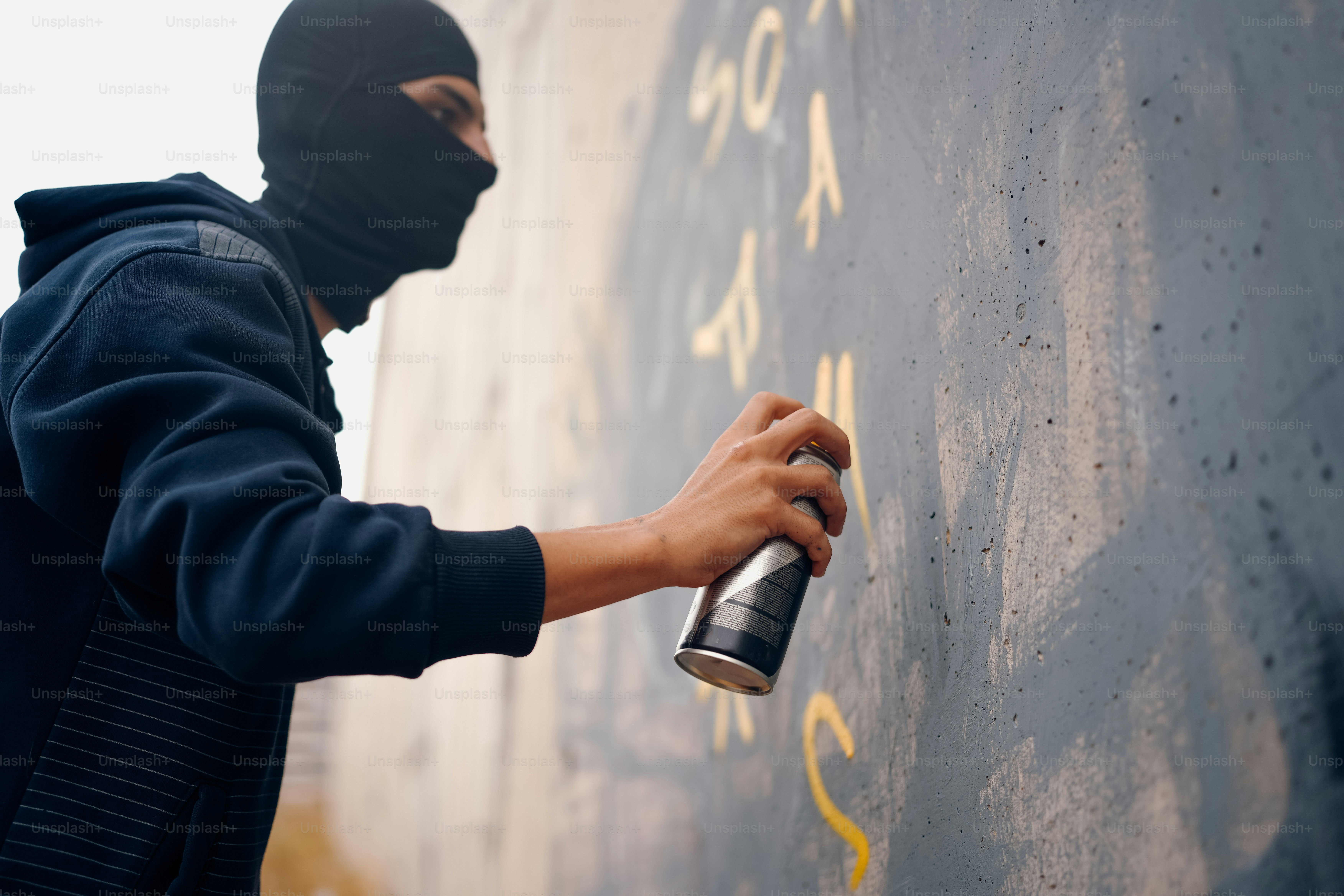 A person wearing a mask spray painting on a wall photo – Tagging Image