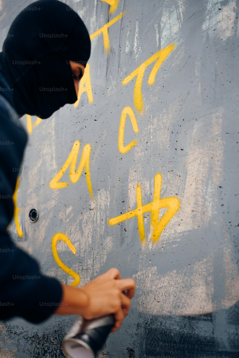 a man in a black hoodie spray painting graffiti on a wall