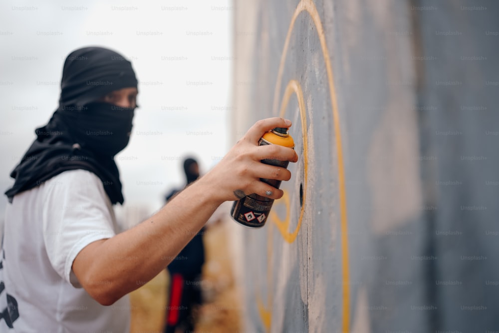 a man in a black head scarf spray painting on a wall