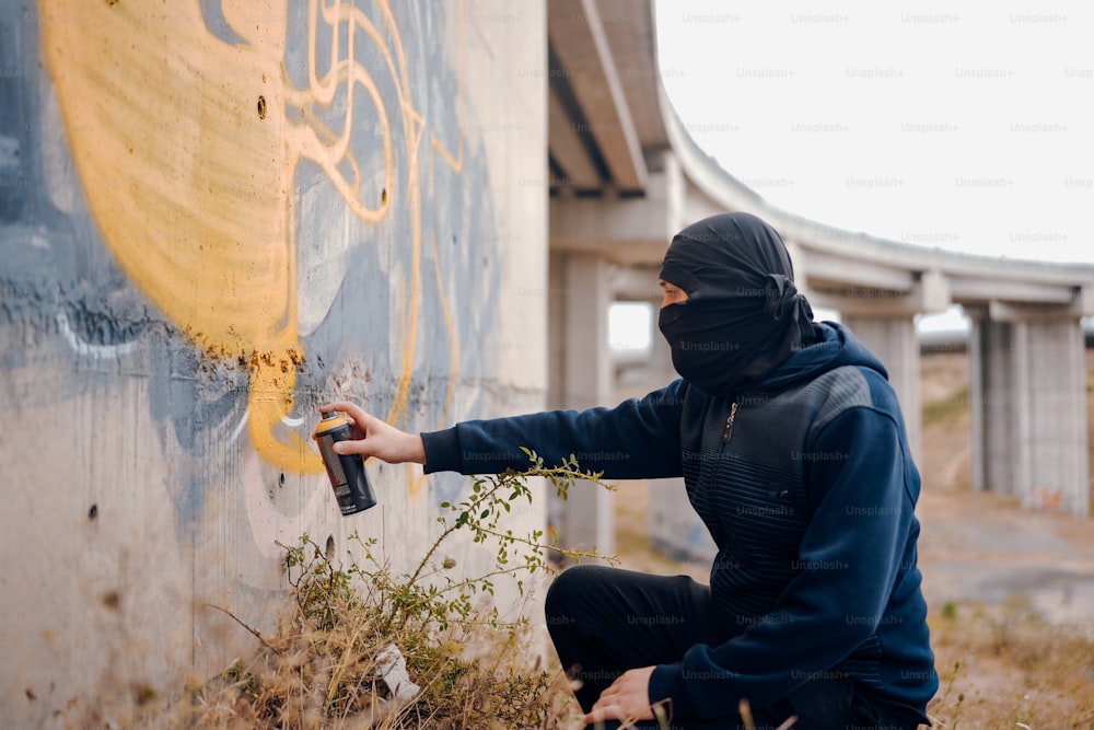 um homem com um spray de capuz preto pintando uma parede