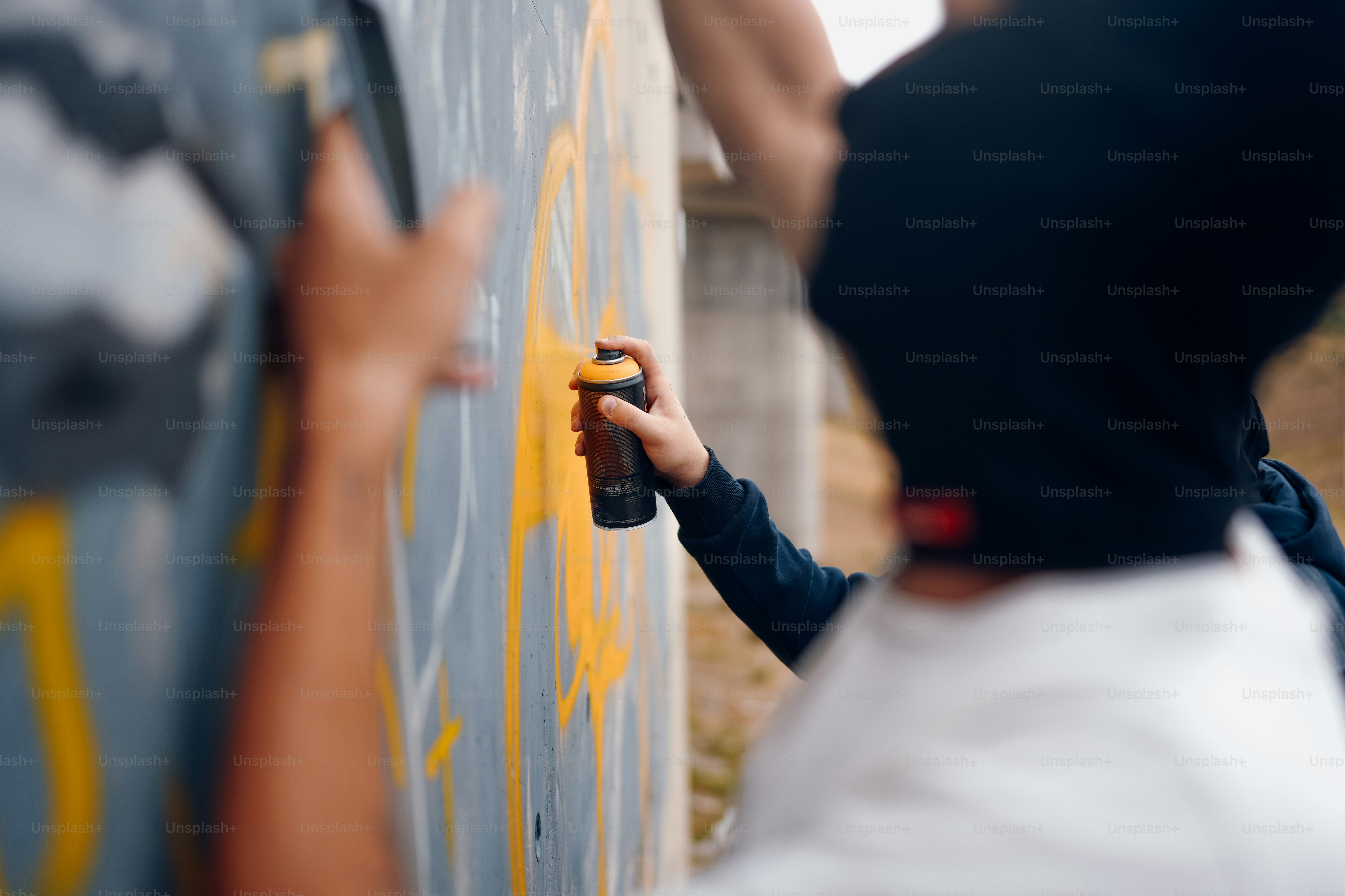 Um homem com um spray de capuz preto pintando grafite em uma parede ...