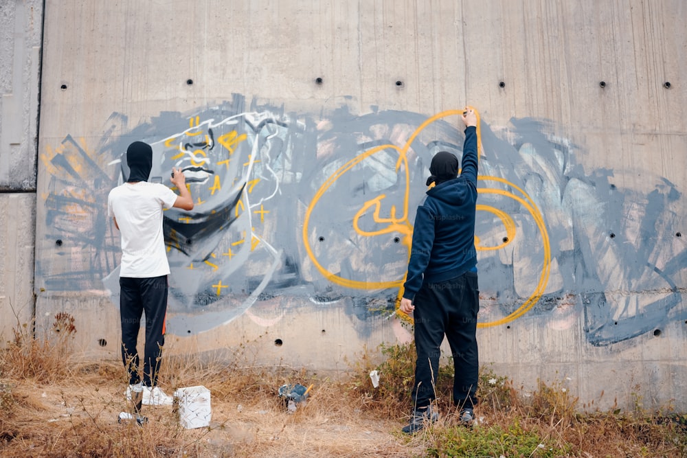 a couple of men standing next to a graffiti covered wall