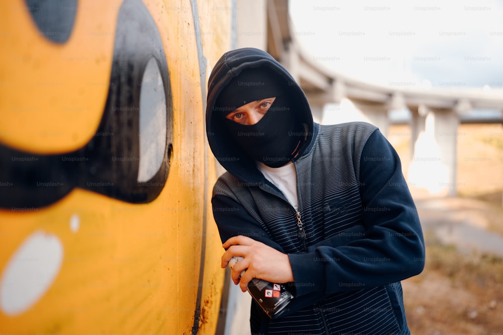 a man in a black mask leaning against a yellow wall