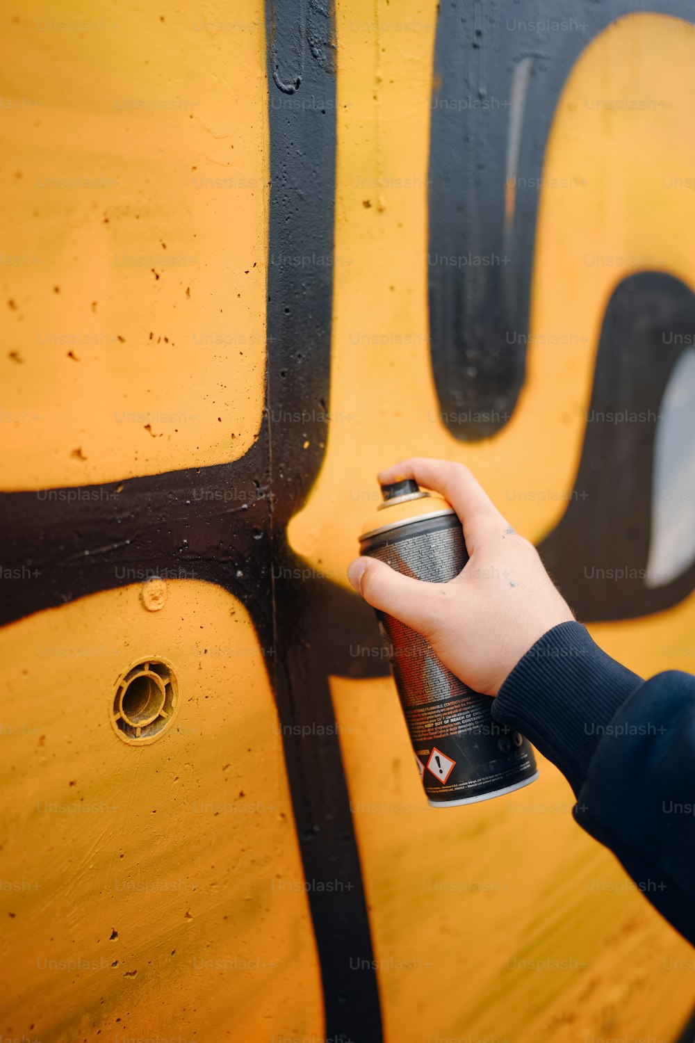 a person spray painting a wall with yellow and black paint