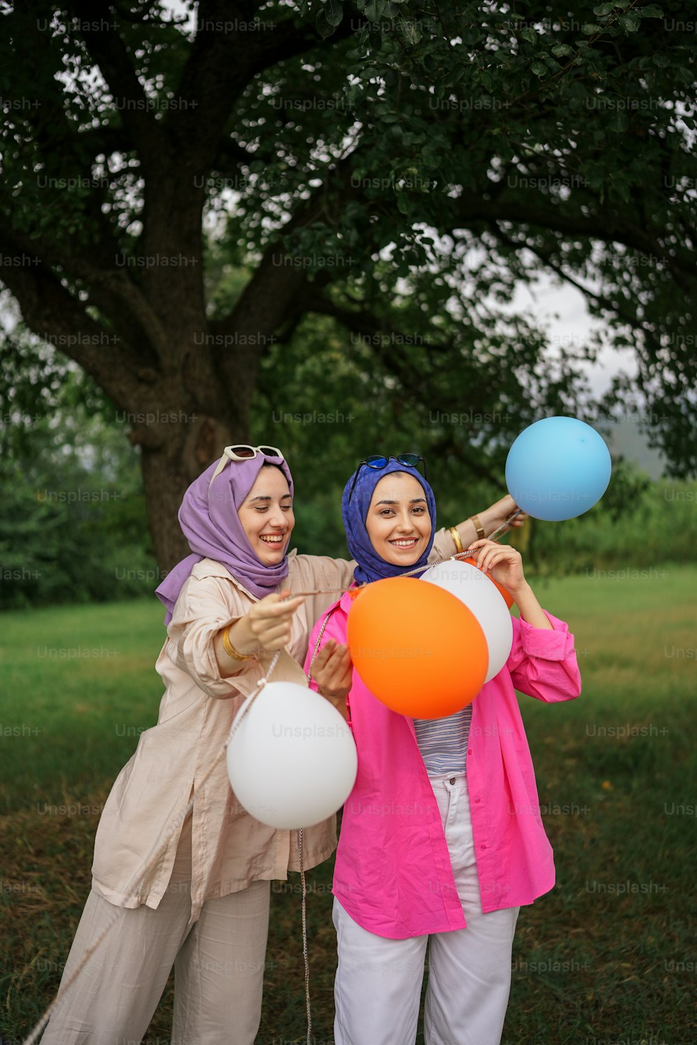 two women in hijabs are holding balloons