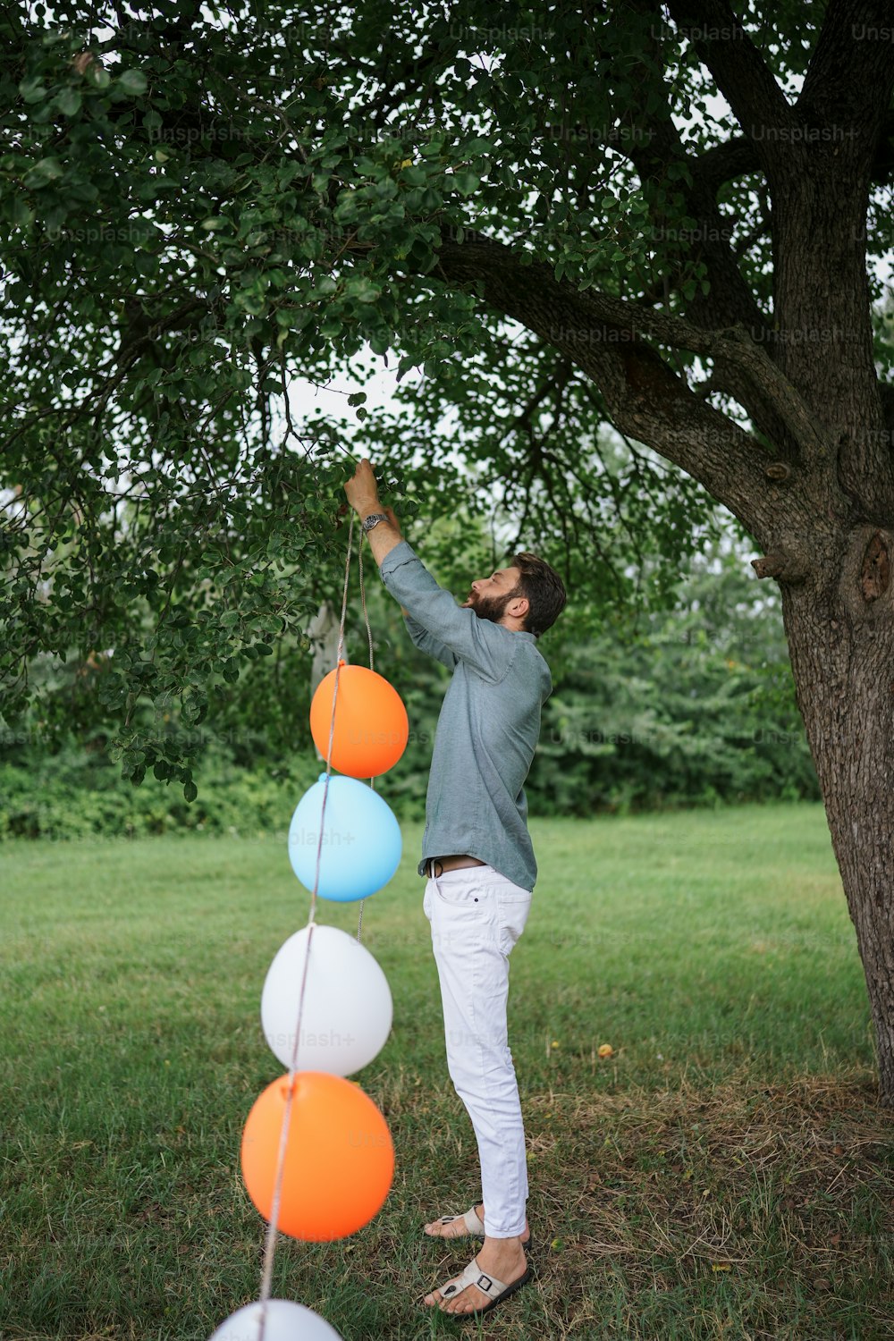 a man standing next to a tree holding a string of balloons