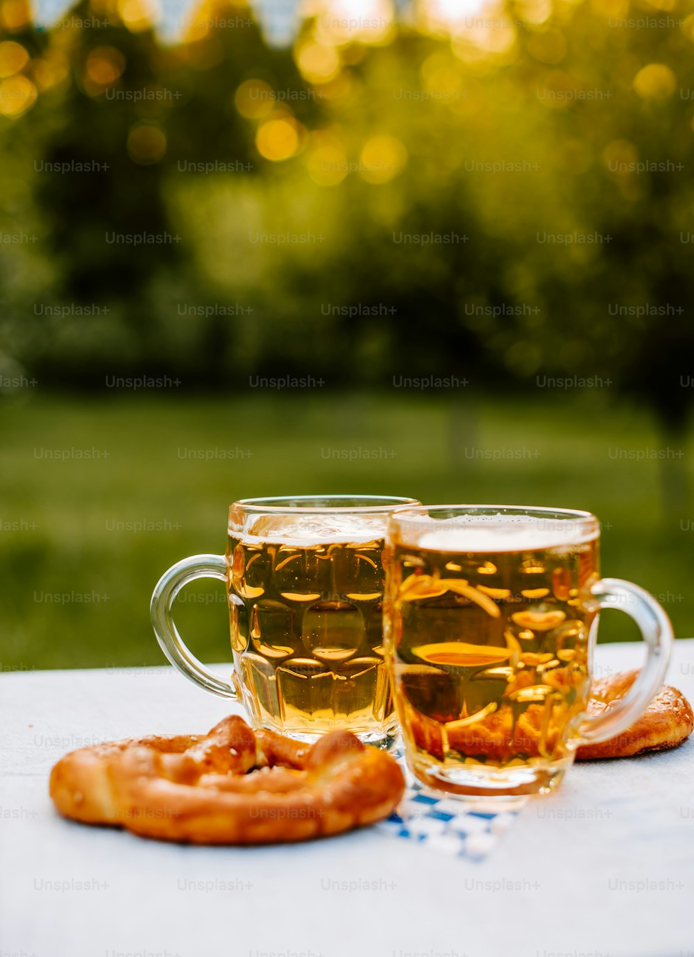 two mugs of beer and a pretzel on a table