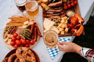 Una persona sosteniendo un vaso de cerveza frente a un plato de comida