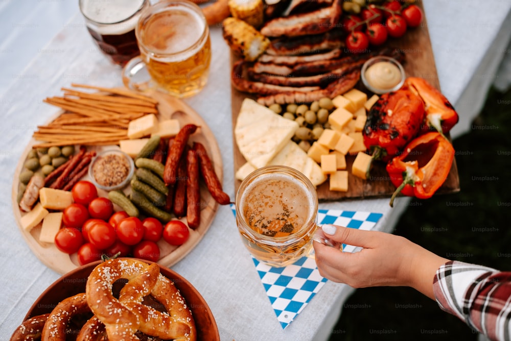 a person holding a glass of beer in front of a platter of food