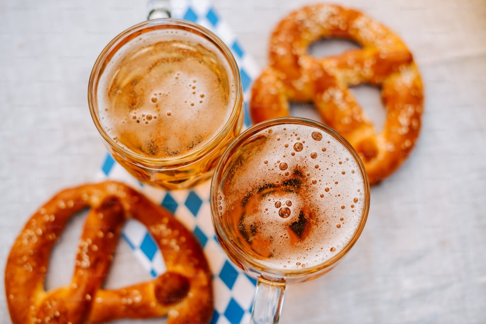 two glasses of beer and pretzels on a table