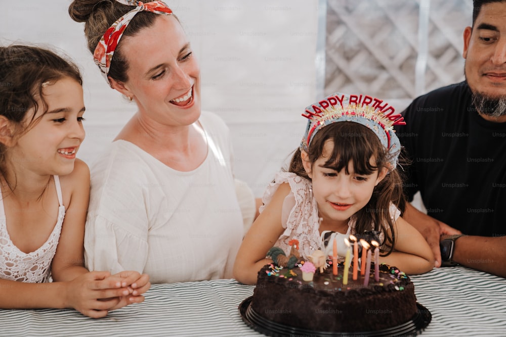 Una mujer y dos niñas sentadas frente a un pastel de cumpleaños