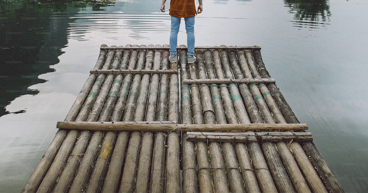 Standing Raft A person standing on a bamboo raft in the middle of a body of water ...