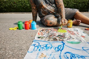 Un uomo seduto a terra che dipinge su un pezzo di carta