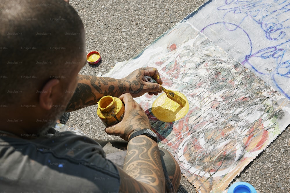 Un homme tatoué peint un tableau sur le sol