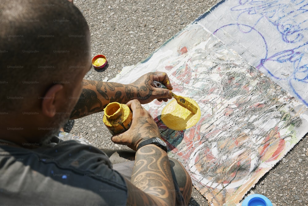 a man with tattoos is painting a picture on the ground