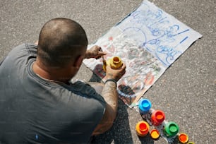 a man sitting on the ground painting on a piece of paper