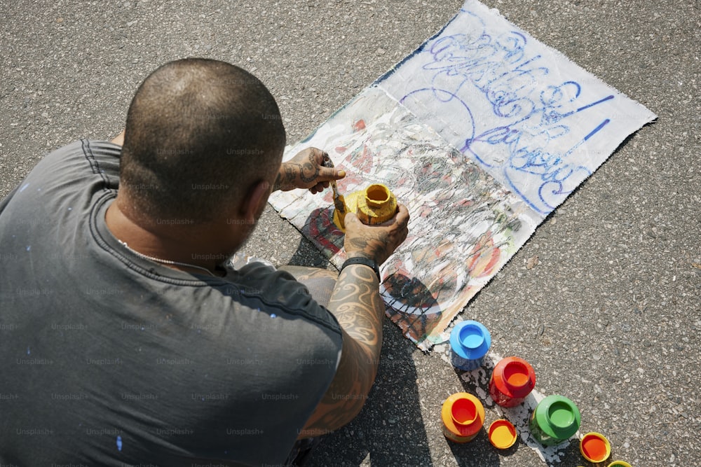 a man sitting on the ground painting on a piece of paper