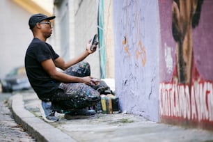 um homem sentado na lateral de um prédio usando um celular