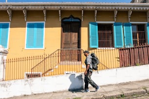 a man walking past a yellow building with blue shutters