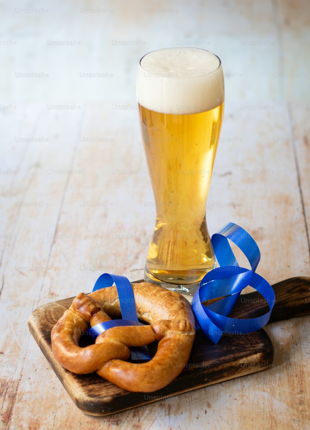 um copo de cerveja e um pretzel em uma tábua de corte