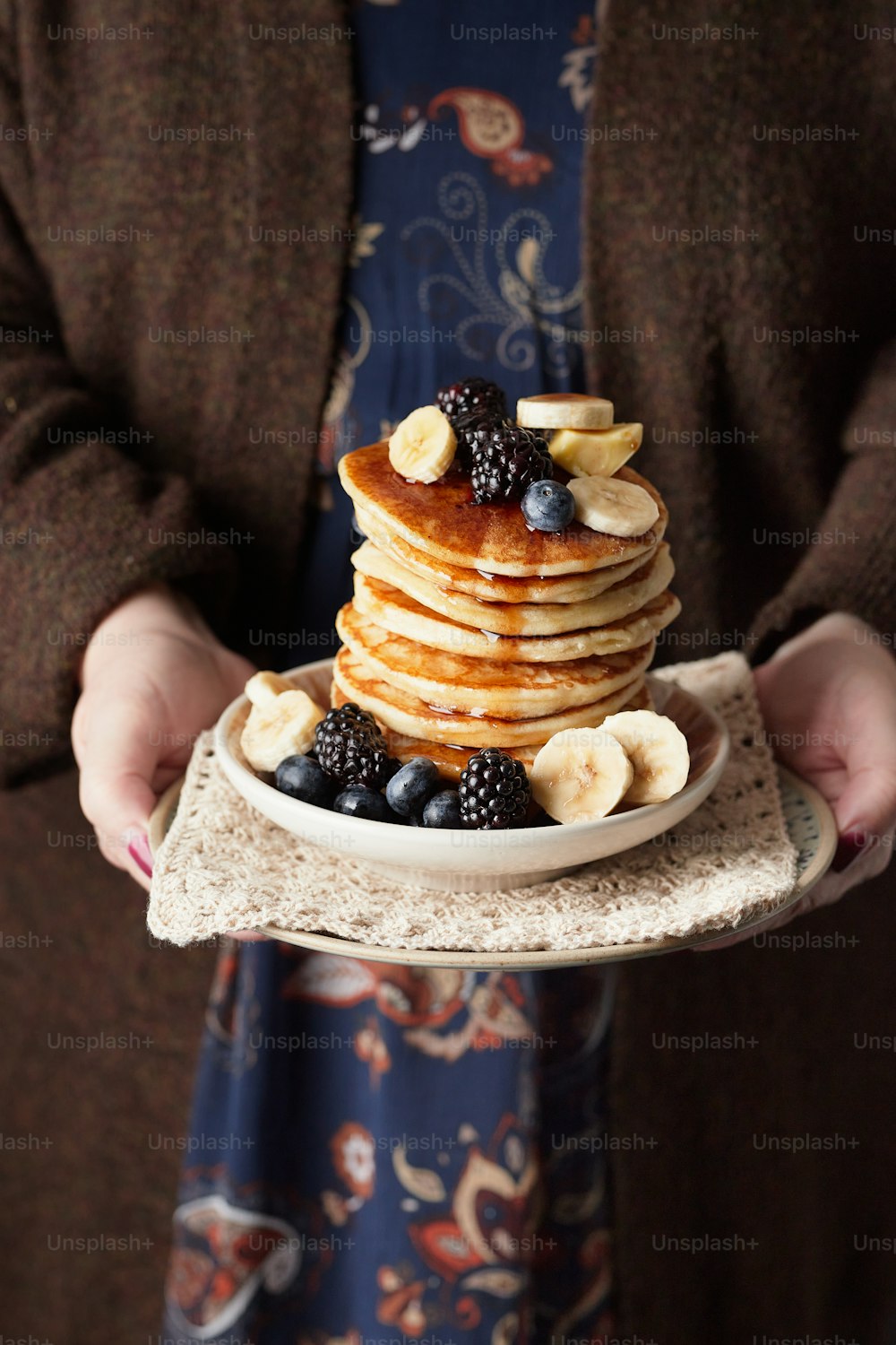 a woman holding a plate of pancakes with bananas and blueberries