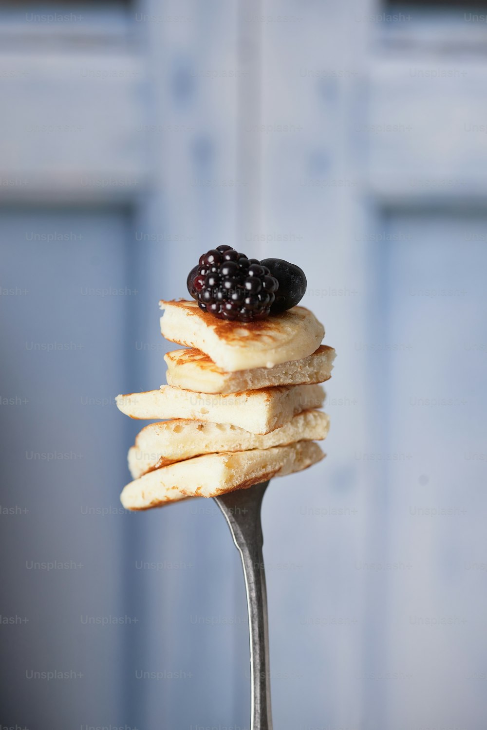 a stack of pancakes on a fork with a blackberry on top