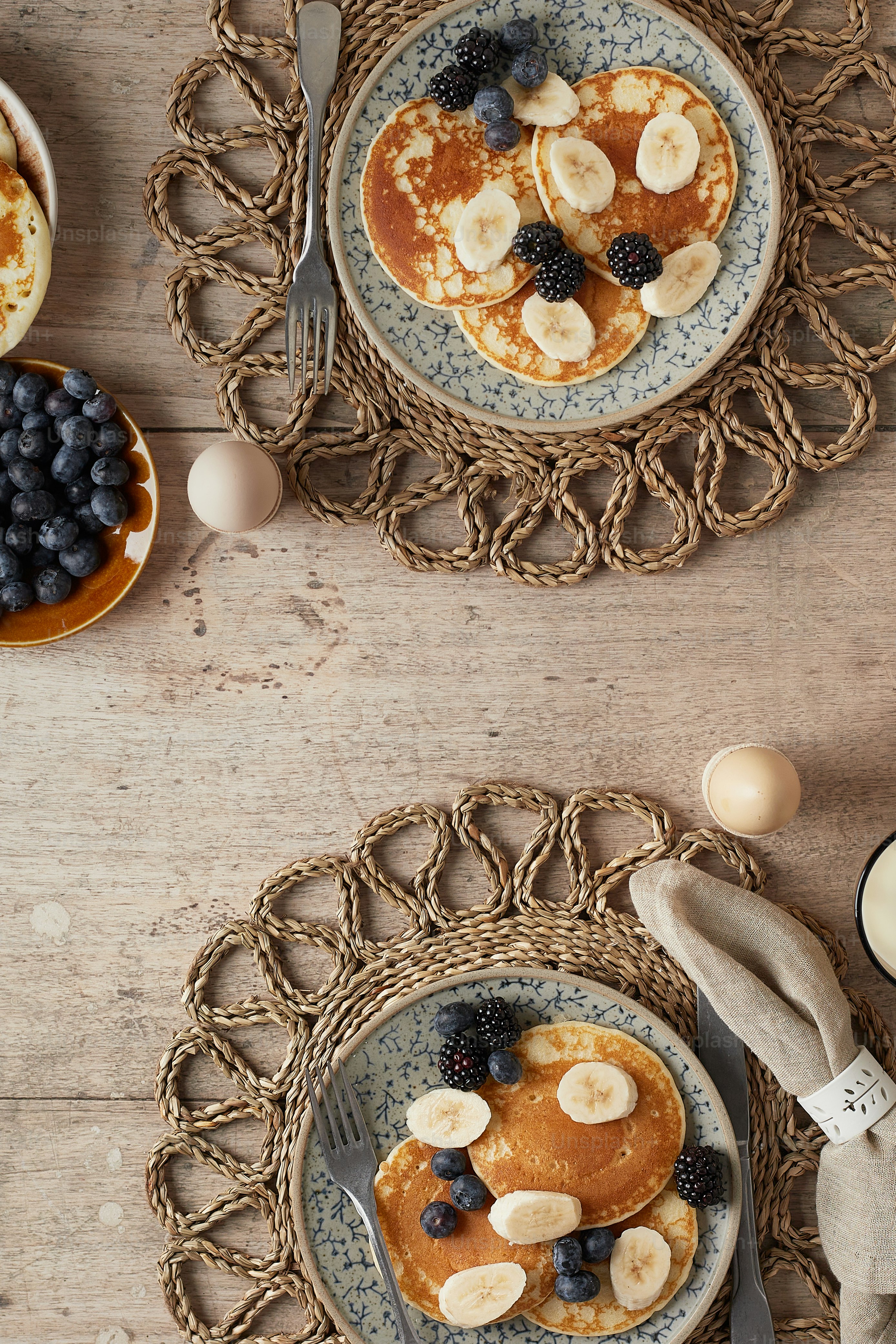 Dos platos de panqueques con plátanos y arándanos