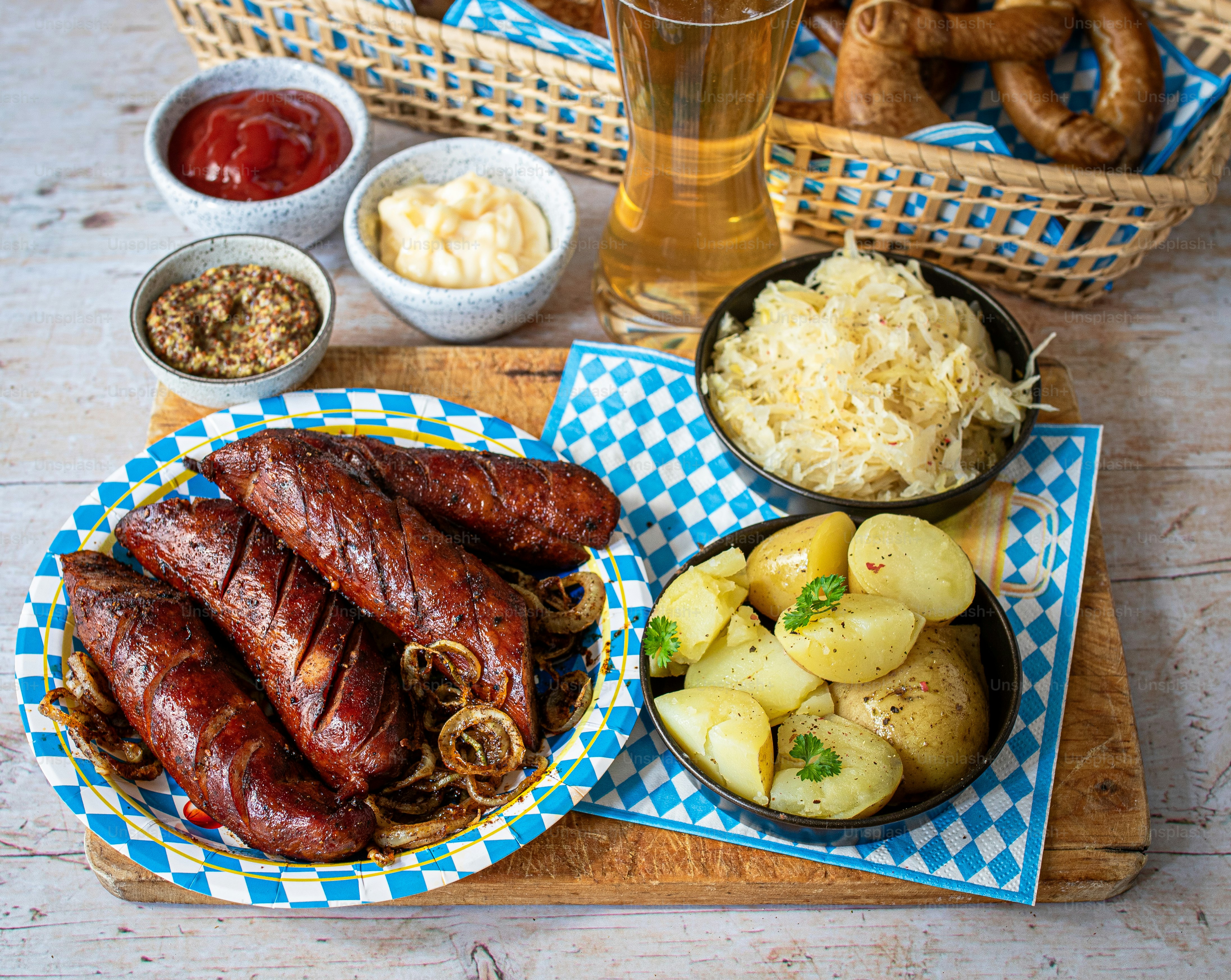 Octoberfest food and drink- sauerkraut, beer, sausage, pretzels potatoes and sauces on wood board.