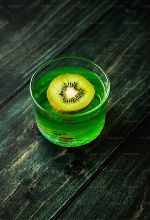 a kiwi cut in half in a green glass on a wooden table