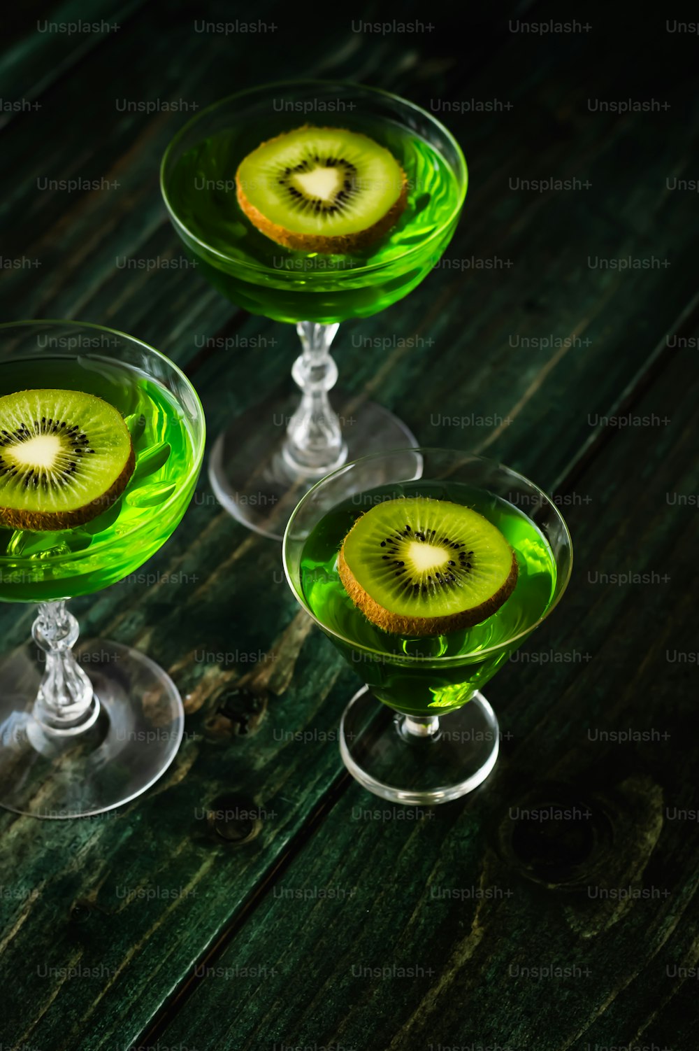 three glasses of green liquid with a kiwi cut in half