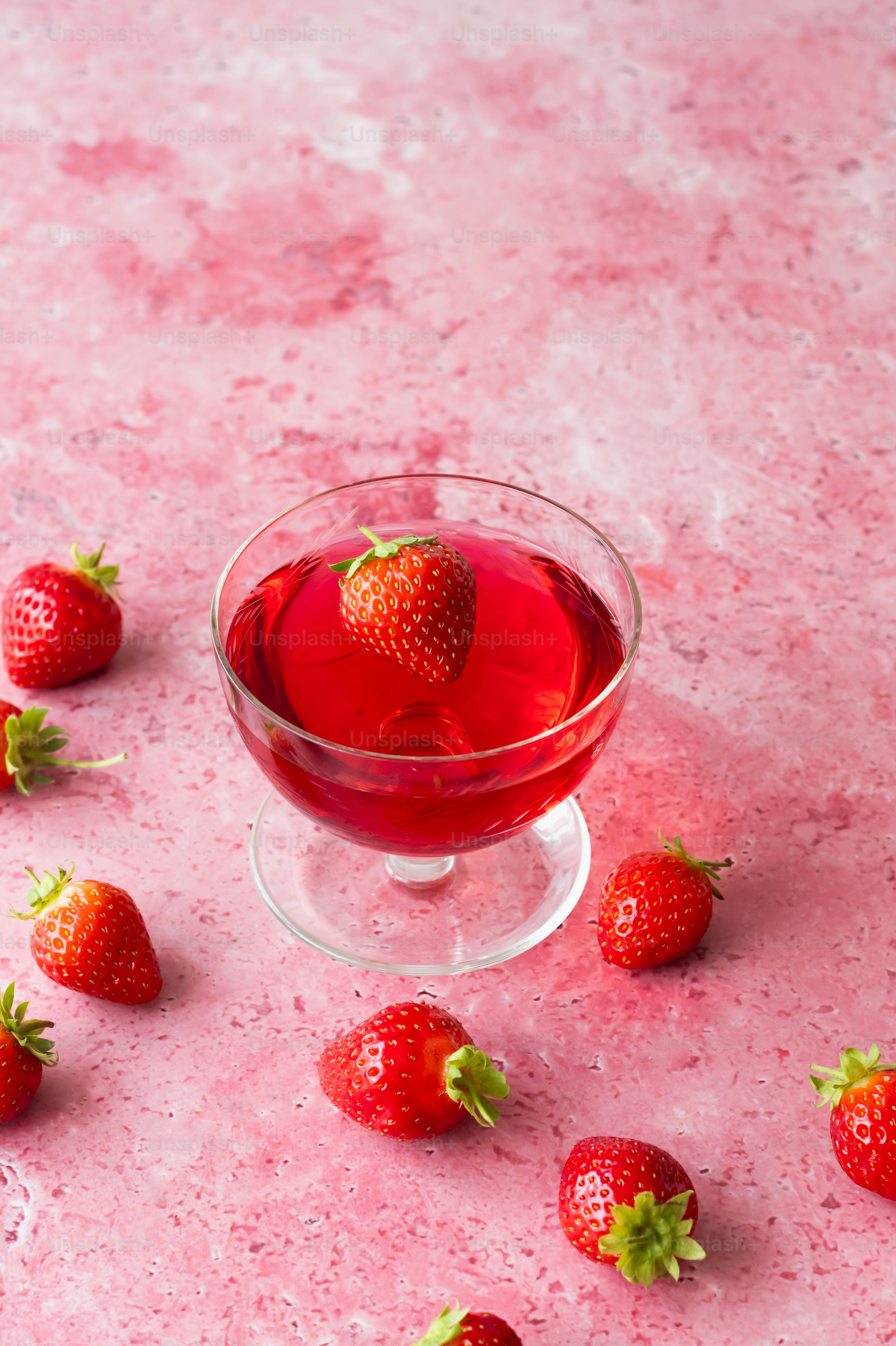 un vaso de líquido rojo con fresas esparcidas a su alrededor