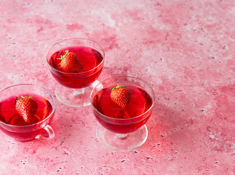 three glasses of red liquid with a strawberry on top