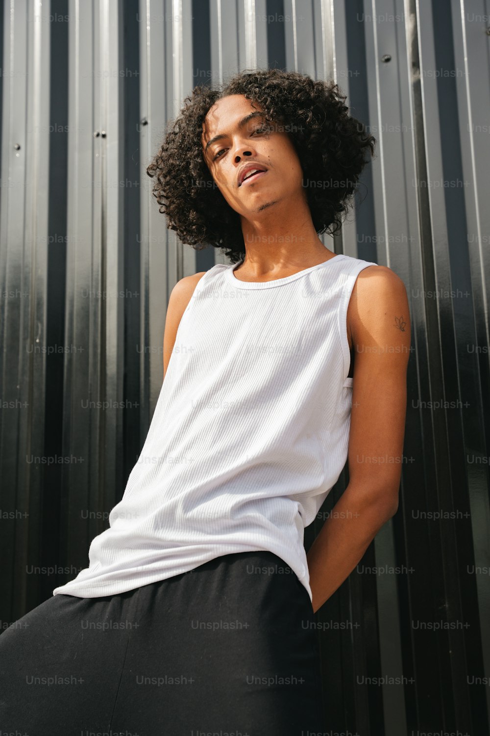 a woman leaning against a metal wall wearing a white tank top