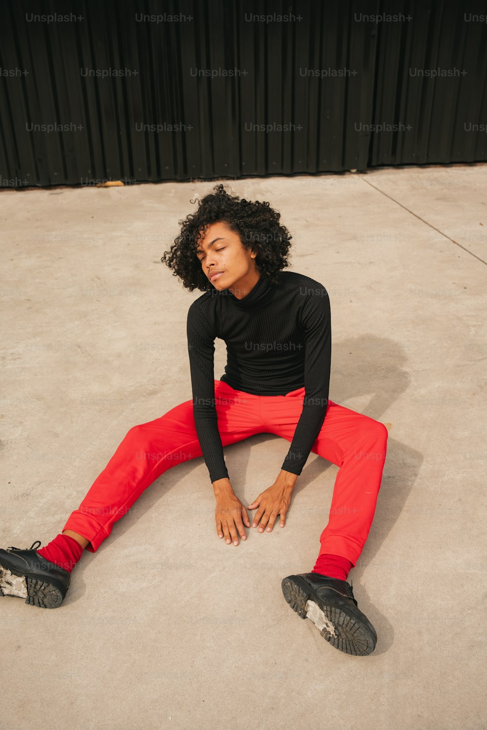 a woman sitting on the ground in a black shirt and red pants