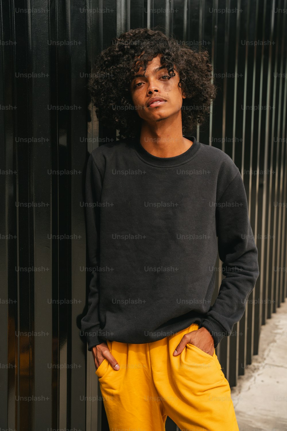 a man with curly hair wearing a black sweater and yellow pants