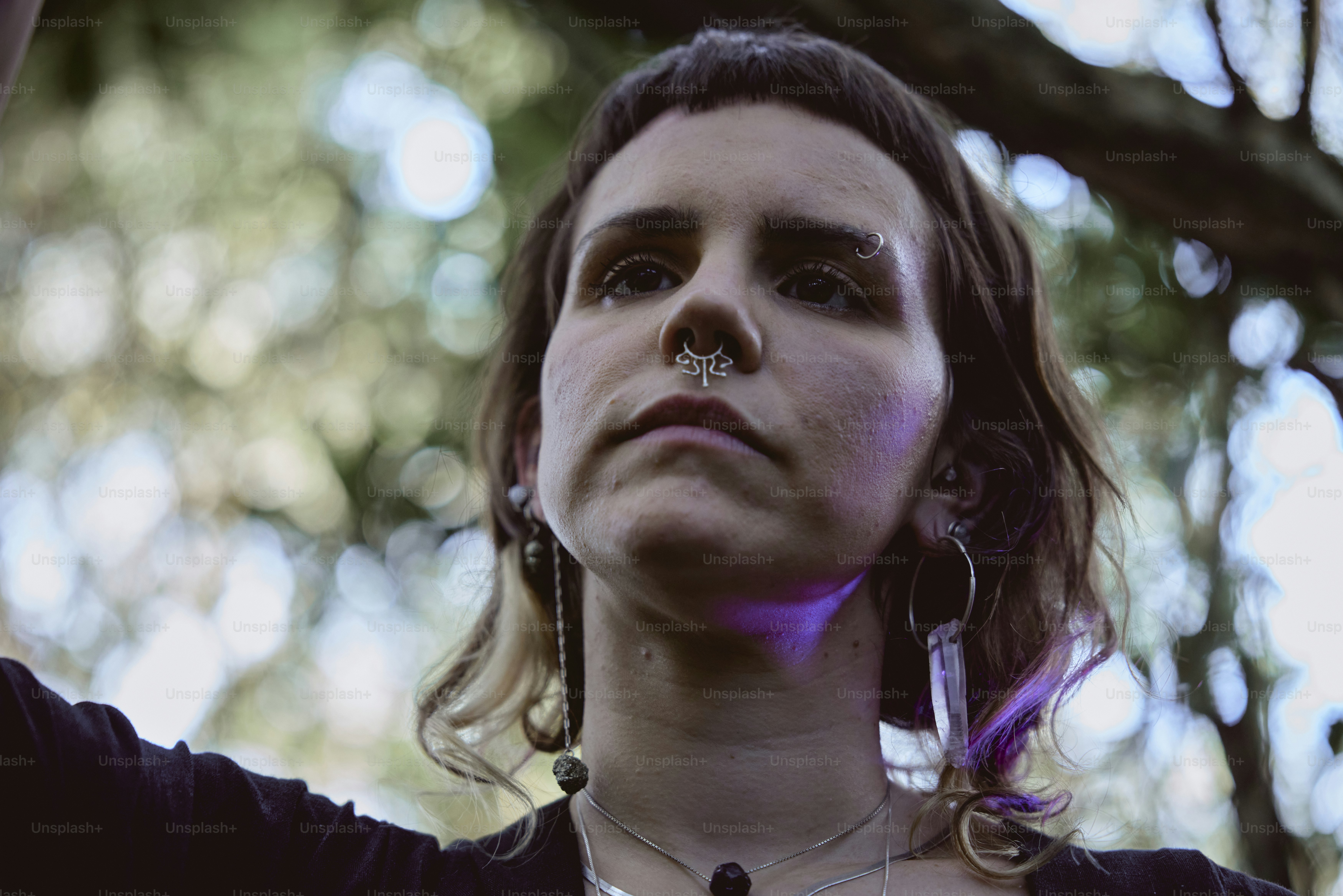 a woman with piercings on her nose standing under a tree