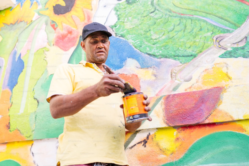 a man holding a can of paint in front of a colorful wall