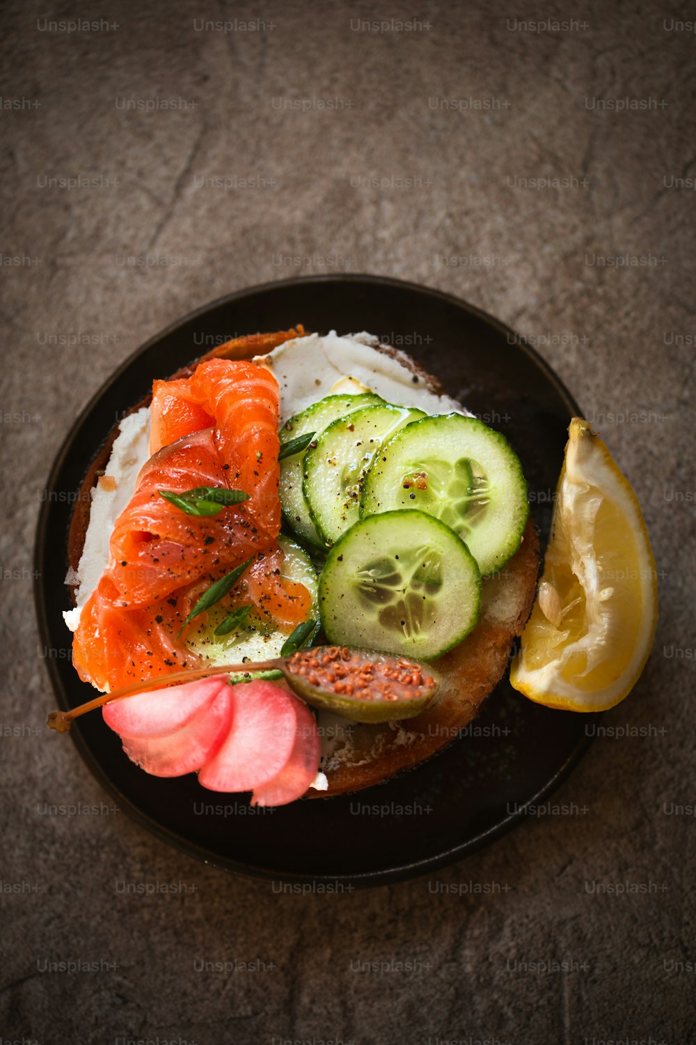 a black plate topped with a sandwich and cucumbers