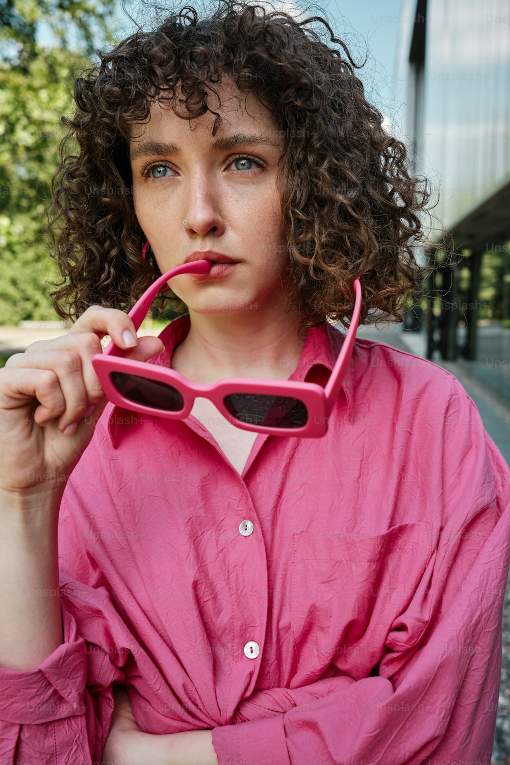 Uma mulher de camisa rosa está segurando um par de óculos escuros