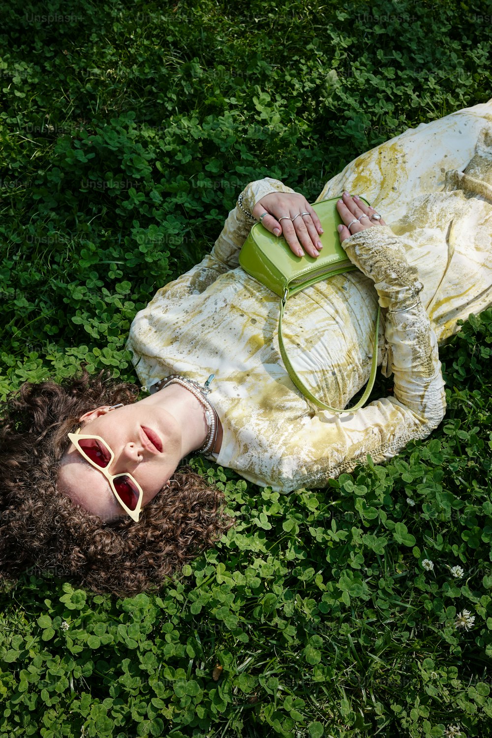 a woman laying in the grass with a green purse